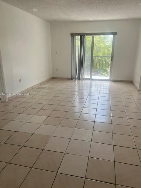 An empty room with light-colored tile flooring and a sliding glass door leading to a balcony — 6965 Harding Ave # 305, Miami Beach FL 33141, MIAMI BEACH, FL