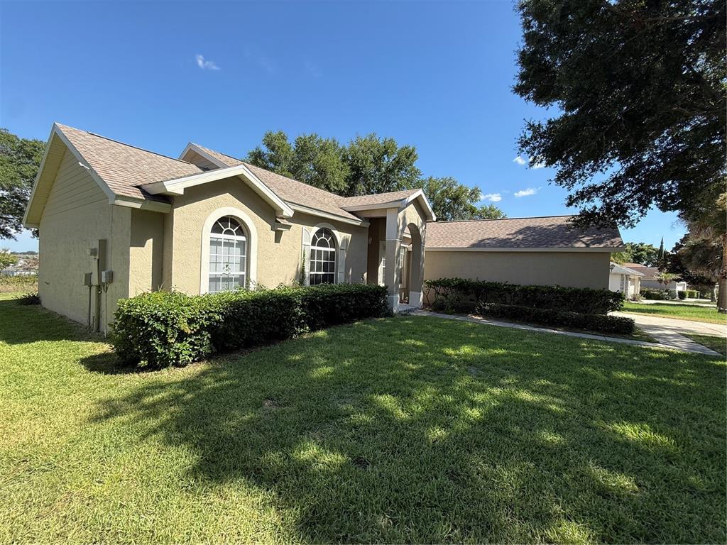 A tan, single-story house with arched windows and a large hedge in the front yard — 2735 CEDARIDGE CIRCLE, CLERMONT, FL