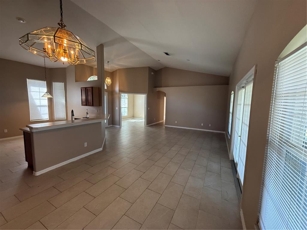 An open-concept living and kitchen area features beige tile flooring and vaulted ceilings — 2735 CEDARIDGE CIRCLE, CLERMONT, FL