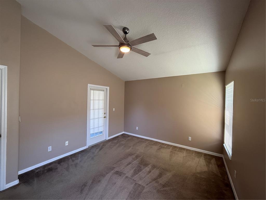 An empty room with tan walls, brown carpet, a ceiling fan, and a glass door — 2735 CEDARIDGE CIRCLE, CLERMONT, FL