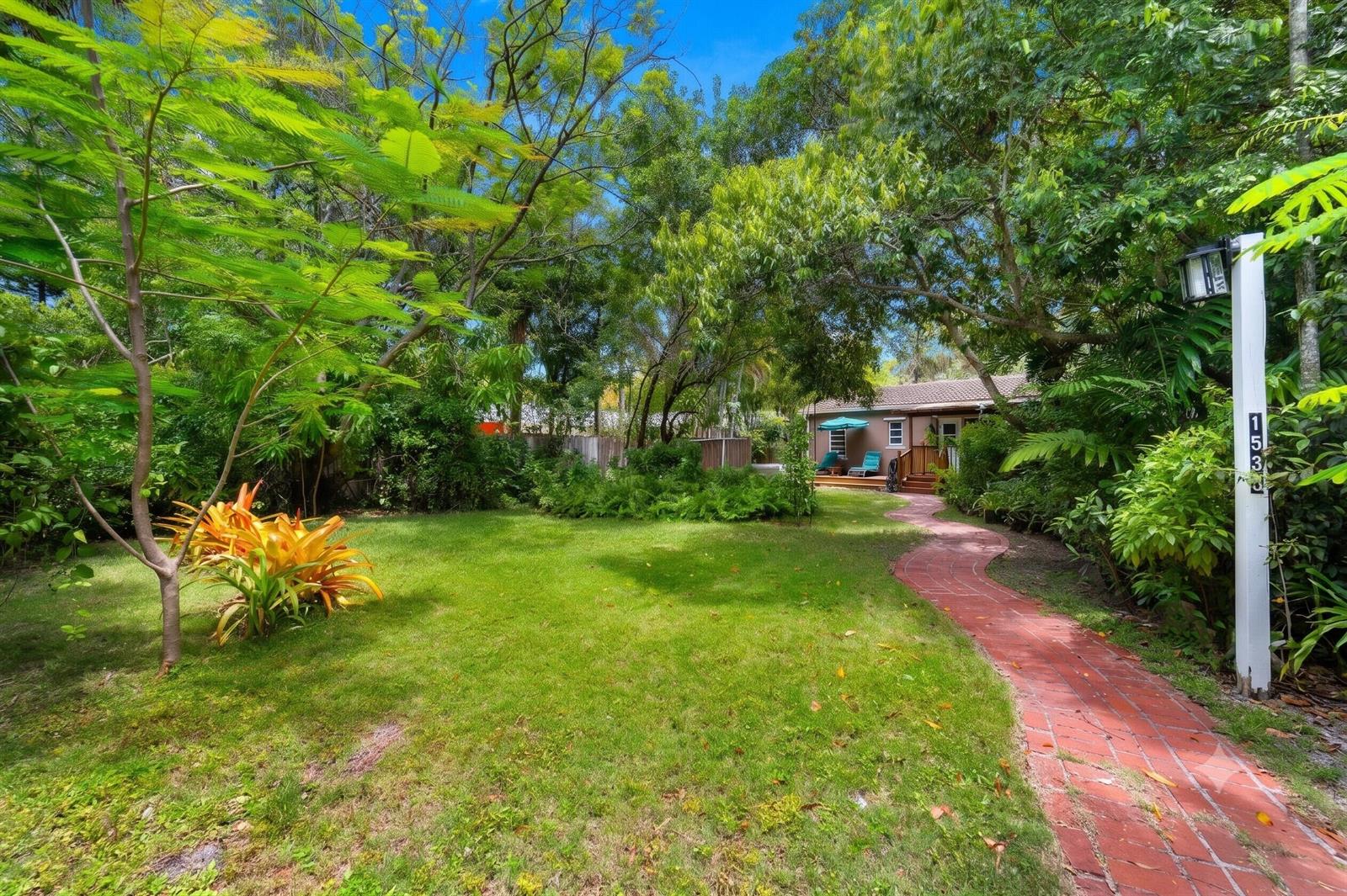 A brick path leads through a lush, tree-filled yard to a small house with a deck — 1535 Dewey Street, Hollywood FL 33020, HOLLYWOOD, FL