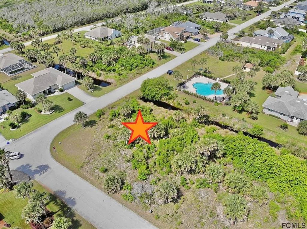 An aerial view shows a vacant, vegetated residential lot marked with a star in a neighborhood — 24 MAHOE DRIVE S, PALM COAST, FL