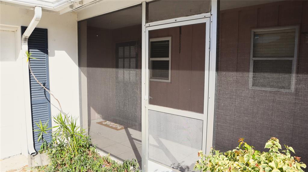 A screened-in porch features a metal door, tiled flooring, and a view of the home — 2118 MICHELE DRIVE, SARASOTA, FL
