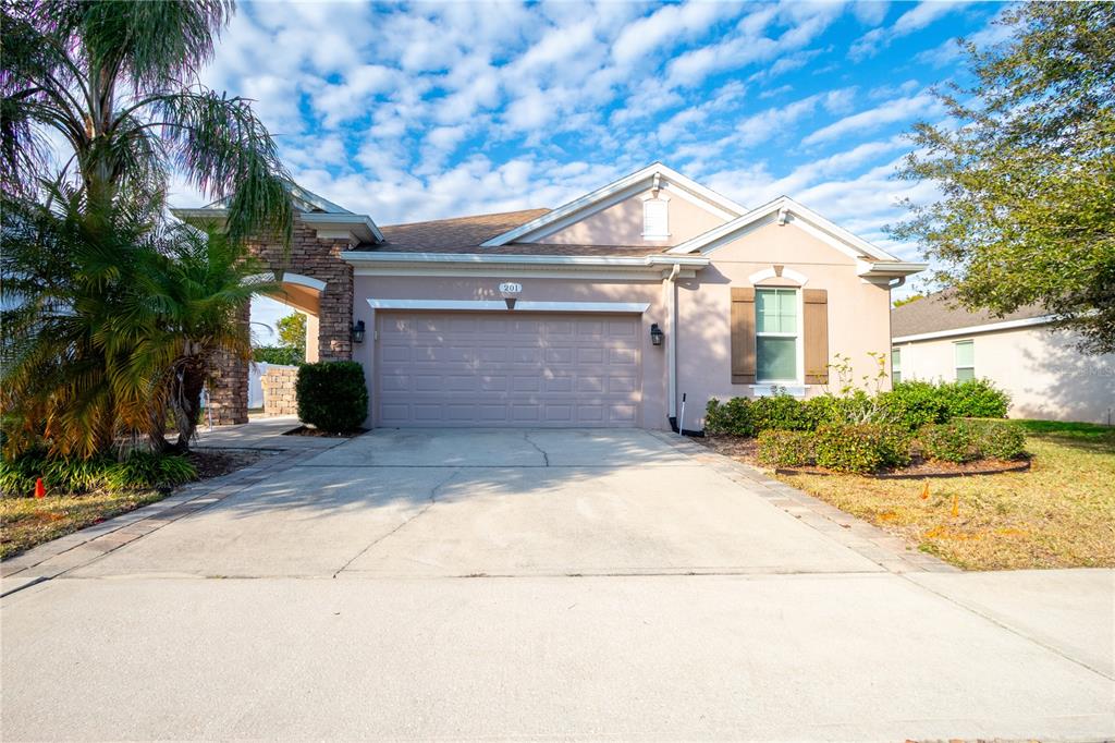 A single-story house with a beige stucco exterior, a two-car garage, and a palm tree — 201 COMPASS ROSE DRIVE, GROVELAND, FL