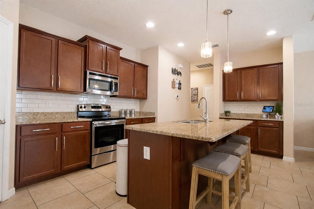 A kitchen featuring dark wood cabinets, granite countertops, a center island, and stainless steel appliances — 201 COMPASS ROSE DRIVE, GROVELAND, FL