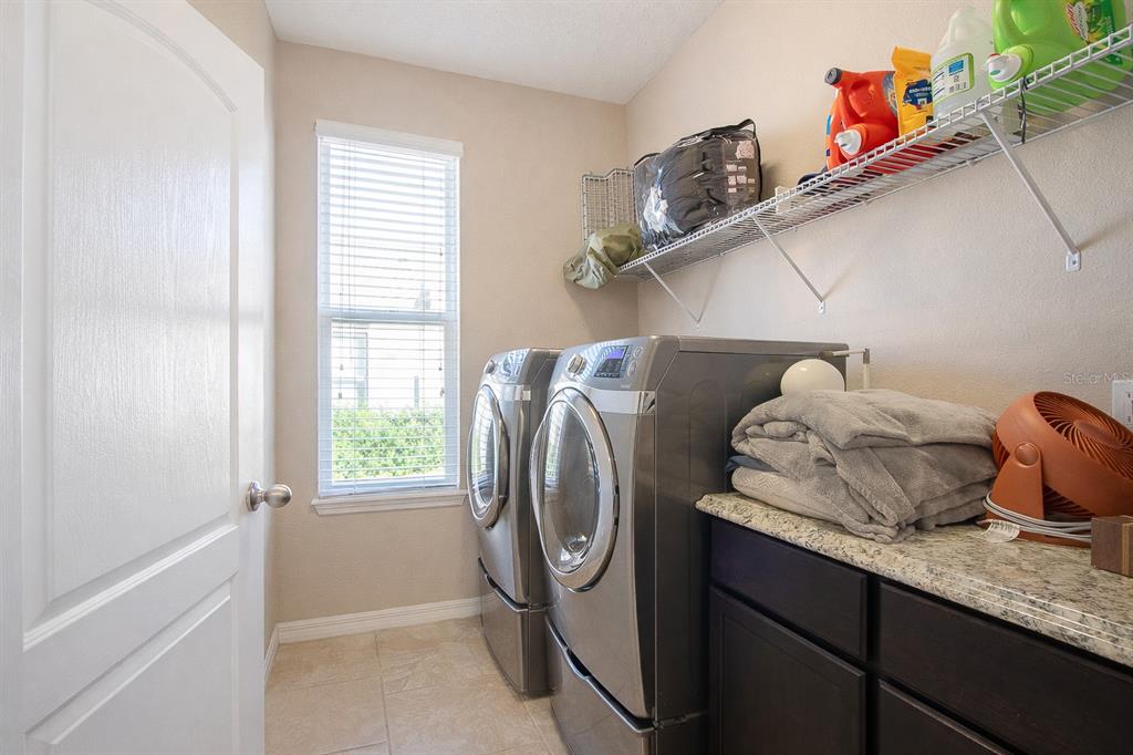 A laundry room features a washer, dryer, dark cabinets, granite countertop, and wire shelving — 201 COMPASS ROSE DRIVE, GROVELAND, FL