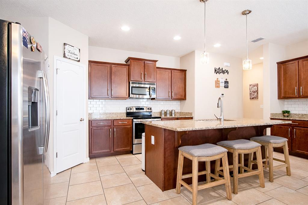 A kitchen with dark wood cabinets, granite countertops, a center island, and three bar stools — 201 COMPASS ROSE DRIVE, GROVELAND, FL