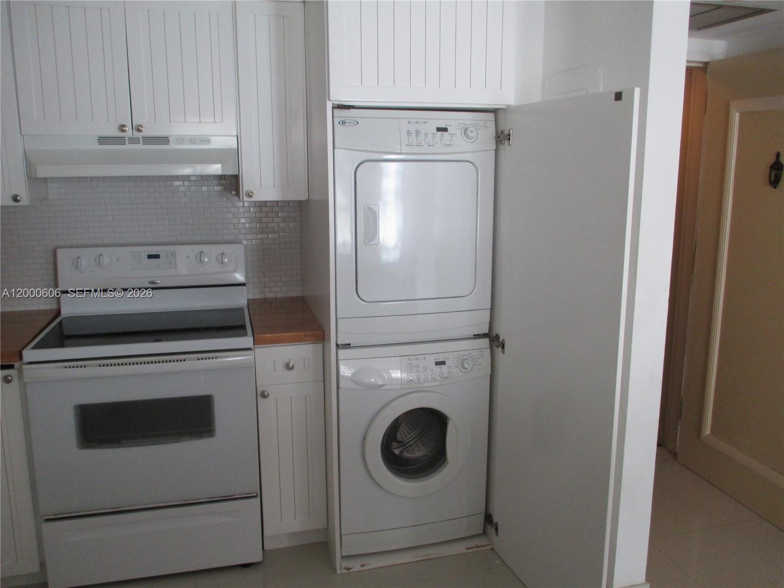 A kitchen features white cabinets, a stove, and a stacked washer and dryer unit — 1865 Brickell Ave # A1207, Miami FL 33129, MIAMI, FL