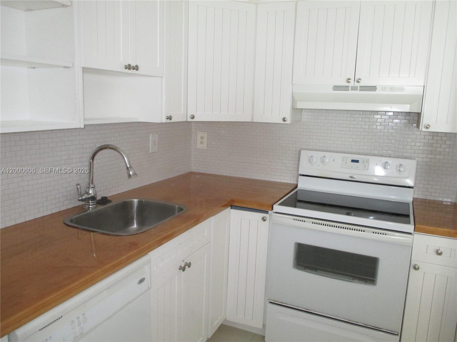 A kitchen features white beadboard cabinets, a wood countertop, a stainless sink, and white appliances — 1865 Brickell Ave # A1207, Miami FL 33129, MIAMI, FL