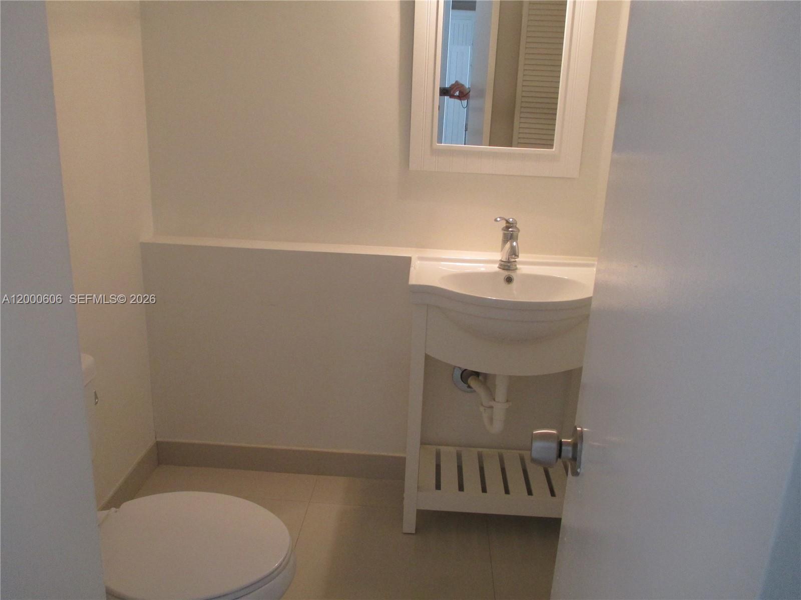 A small bathroom features a white pedestal sink, a toilet, and a wall-mounted mirror — 1865 Brickell Ave # A1207, Miami FL 33129, MIAMI, FL