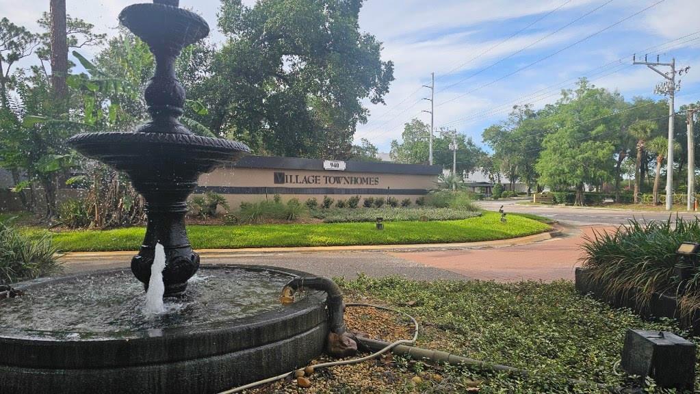 A tiered outdoor fountain sits in front of a sign for Village Townhomes — 940 DOUGLAS AVENUE UNIT 212, ALTAMONTE SPRINGS, FL