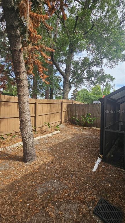 A fenced backyard features a large tree, scattered leaves, and a portion of a screened enclosure — 940 DOUGLAS AVENUE UNIT 212, ALTAMONTE SPRINGS, FL