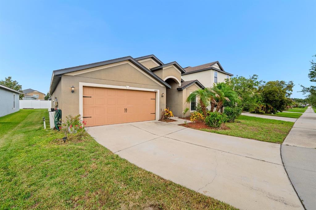 A tan stucco house with a two-car garage and a concrete driveway under a blue sky — 11837 THICKET WOOD DRIVE, RIVERVIEW, FL