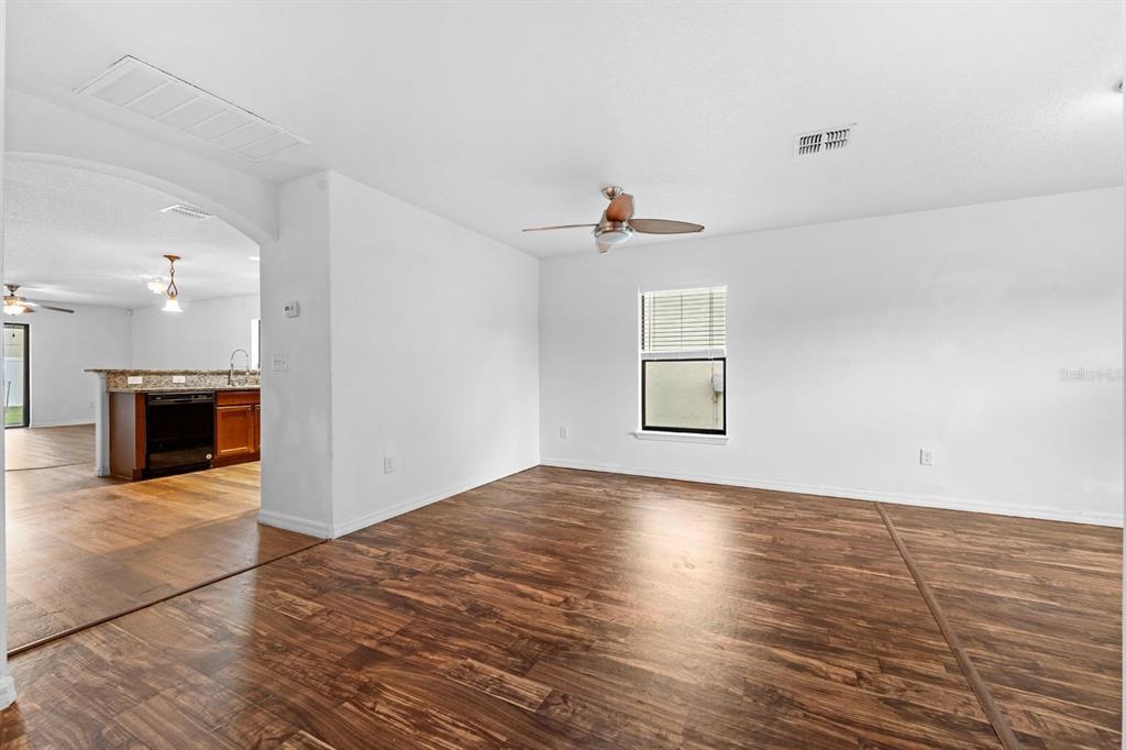 An empty room with wood-look flooring, a ceiling fan, and a view into the kitchen — 11837 THICKET WOOD DRIVE, RIVERVIEW, FL
