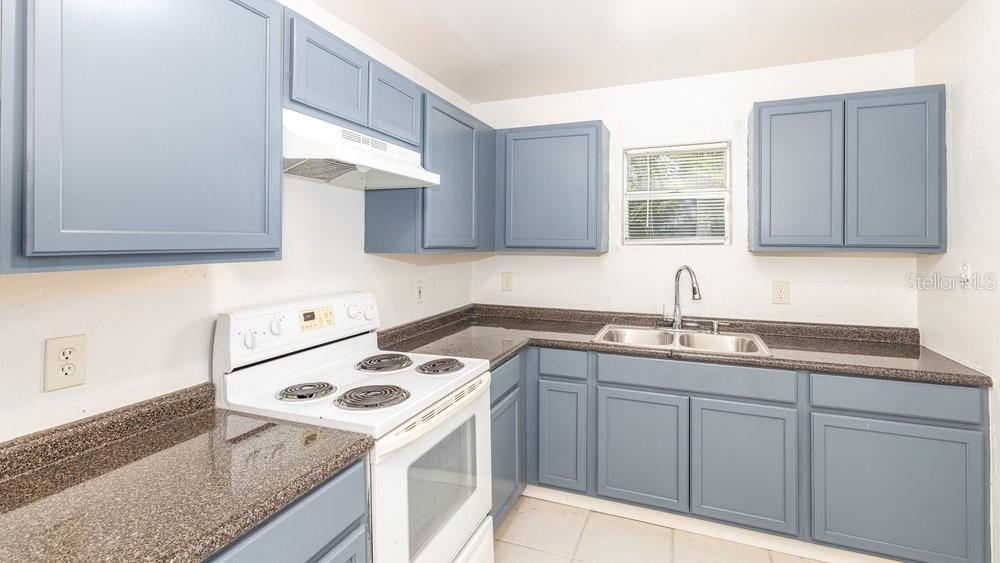 A kitchen features blue cabinets, dark granite countertops, and a white electric stove — 31128 LOCHMORE CIRCLE, SORRENTO, FL