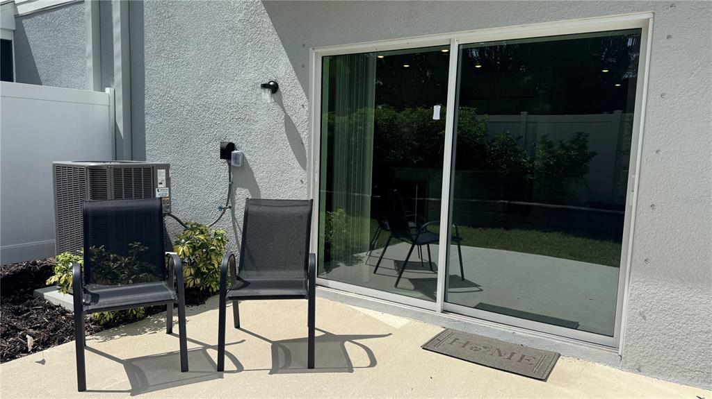 A patio with two black chairs, a sliding glass door, and an air conditioning unit — 9024 DRIVEN SNOW STREET, SARASOTA, FL