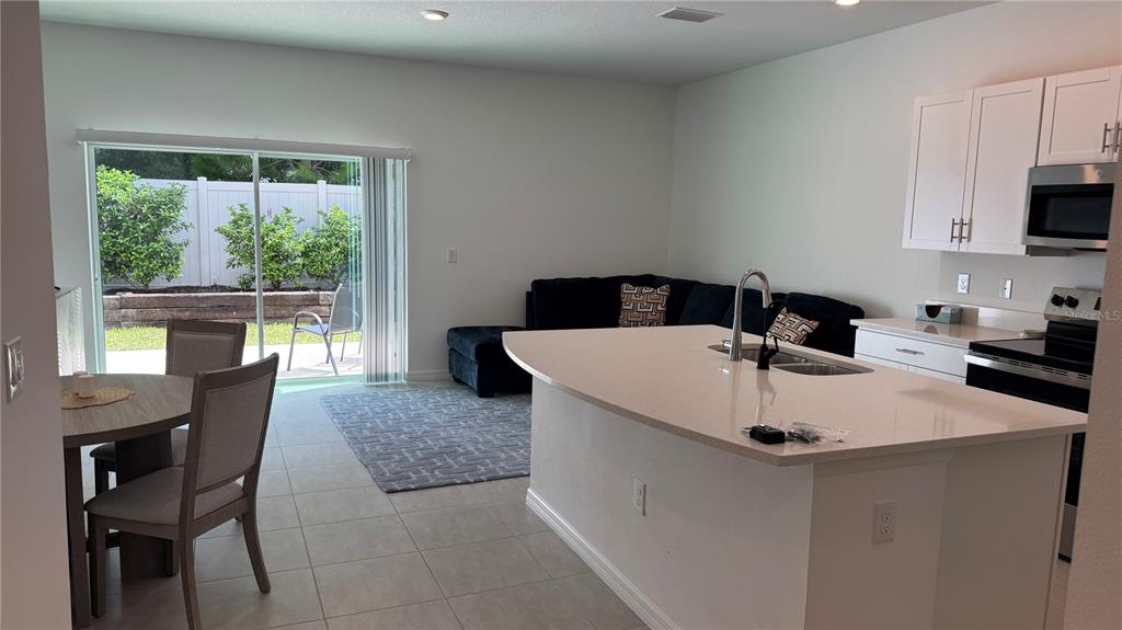 An open-concept kitchen and living area features a large island, white cabinets, and sliding doors — 9024 DRIVEN SNOW STREET, SARASOTA, FL