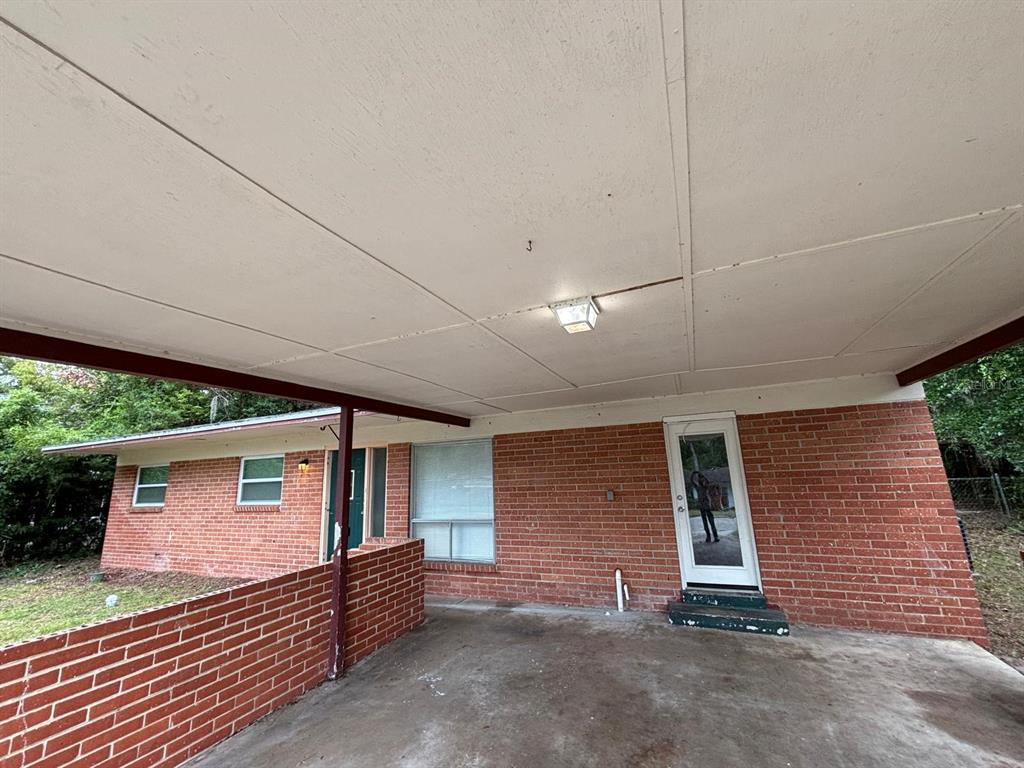 A brick house exterior features a covered carport with a light fixture and a door — 1121 NE 13TH AVENUE, OCALA, FL