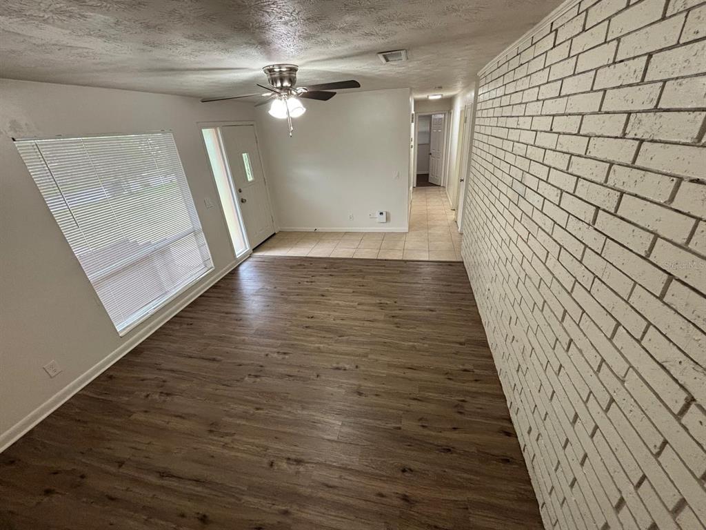 A living room features wood-look flooring, a white brick accent wall, and a ceiling fan — 1121 NE 13TH AVENUE, OCALA, FL