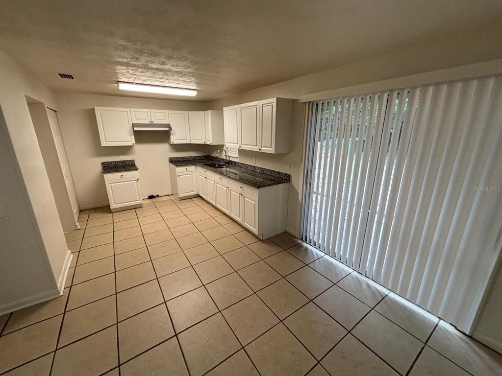 A kitchen with white cabinets, dark granite countertops, tile flooring, and a sliding glass door — 1121 NE 13TH AVENUE, OCALA, FL