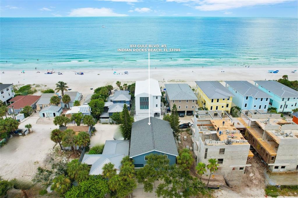 An aerial view shows a blue house near the beach with neighboring properties and construction — 812 GULF BLVD UNIT 3, INDIAN ROCKS BEACH, FL