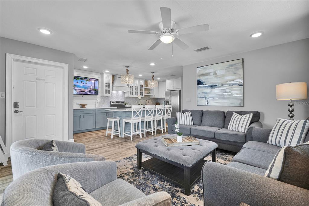 A living room and kitchen open-concept space featuring gray furniture, wood flooring, and white cabinetry — 812 GULF BLVD UNIT 3, INDIAN ROCKS BEACH, FL