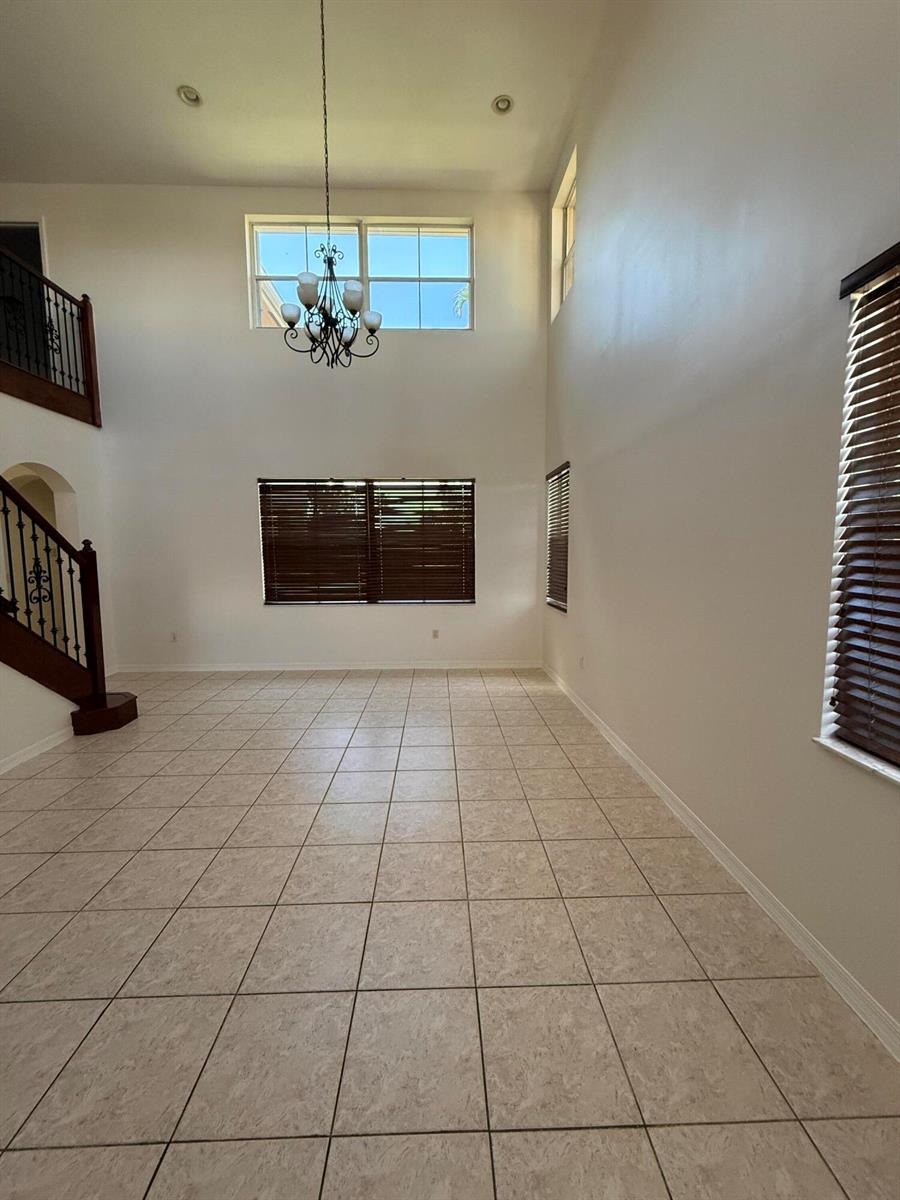 A spacious living room with high ceilings, tile flooring, a chandelier, and a staircase — 12631 SW 28th Street, Miramar FL 33027, MIRAMAR, FL