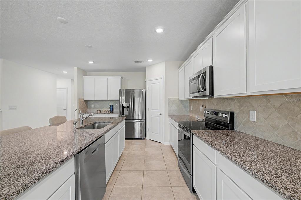 A kitchen features white cabinets, granite countertops, stainless steel appliances, and tile flooring — 3891 CAPRI COAST DRIVE, PLANT CITY, FL