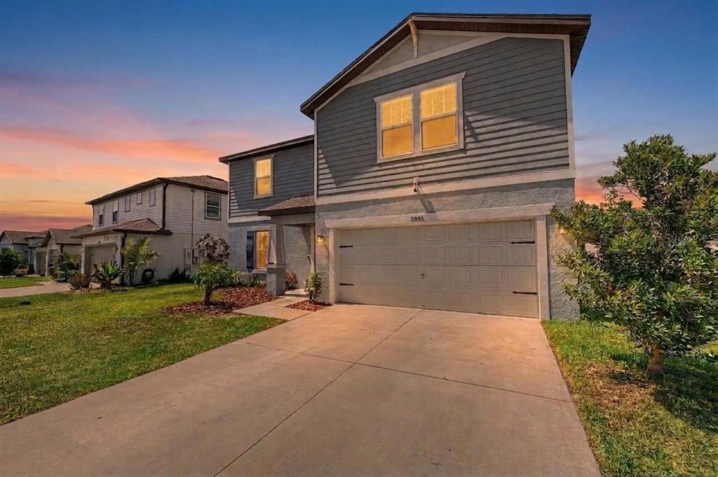 A two-story house with gray siding, a two-car garage, and a concrete driveway at sunset — 3891 CAPRI COAST DRIVE, PLANT CITY, FL