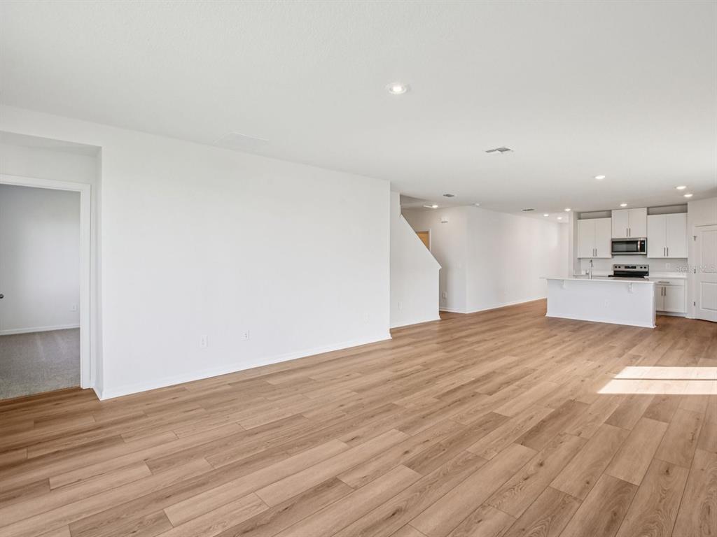 An open-concept living area features light wood-look flooring, white walls, and a modern kitchen — 1718 COOLRIDGE PLACE, ZEPHYRHILLS, FL