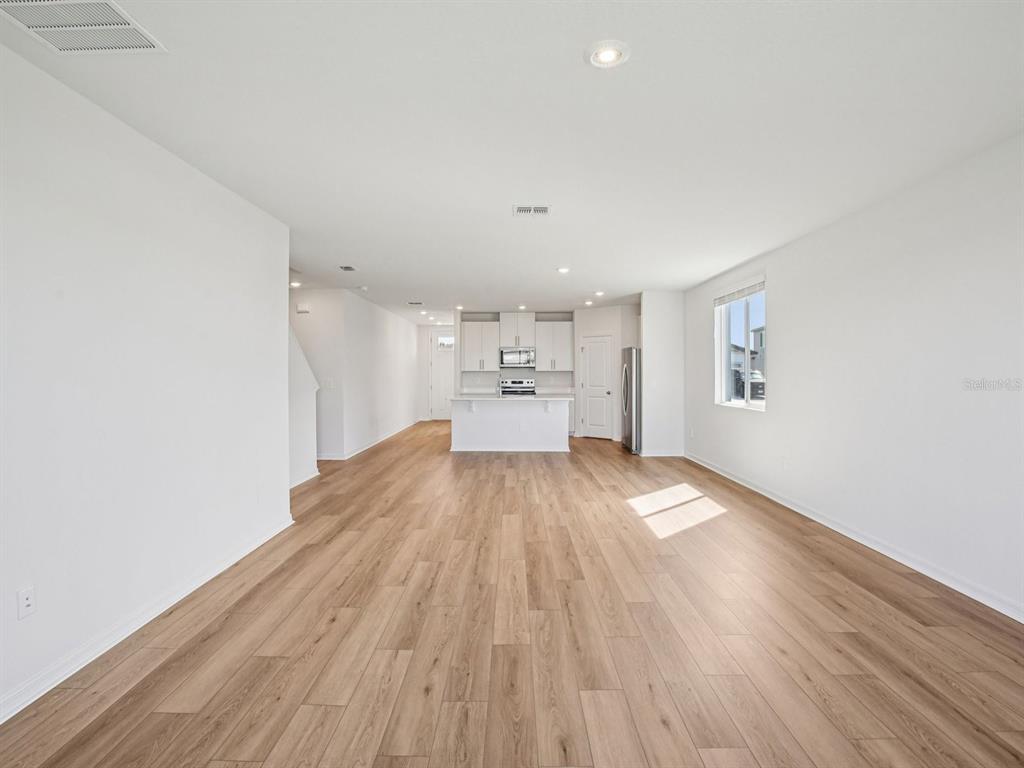 An open-concept living area features light wood-look flooring, white walls, and a modern kitchen — 1718 COOLRIDGE PLACE, ZEPHYRHILLS, FL