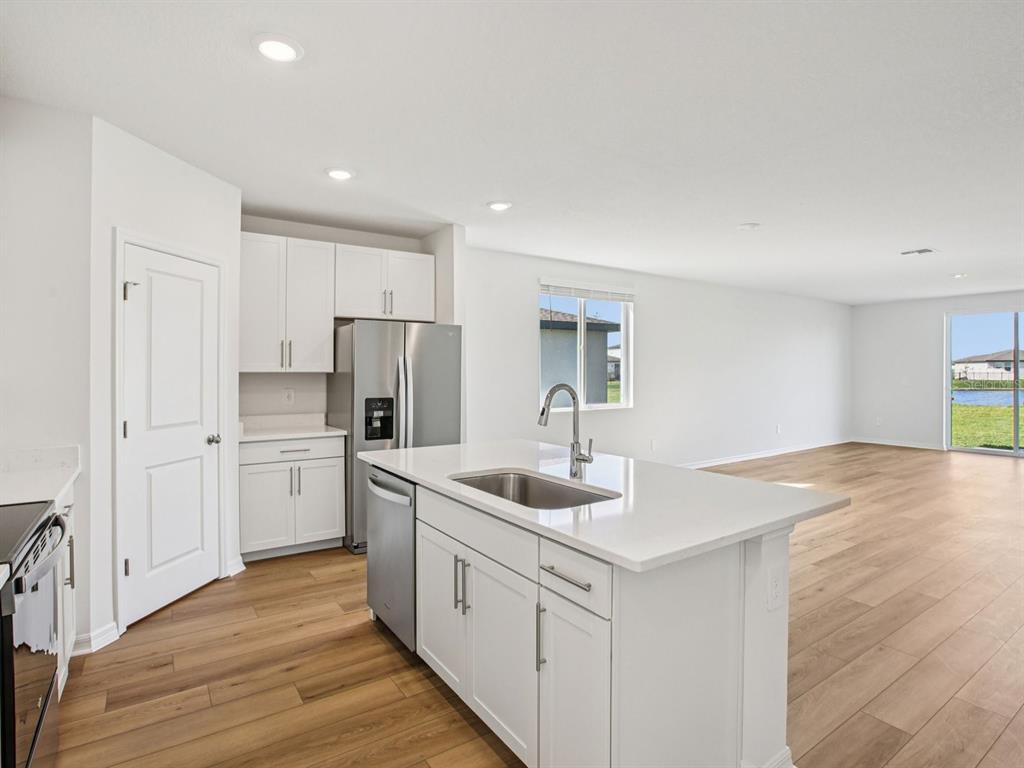 A modern kitchen features white cabinets, stainless steel appliances, a center island, and wood flooring — 1718 COOLRIDGE PLACE, ZEPHYRHILLS, FL