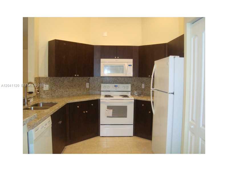 A kitchen features dark wood cabinets, granite countertops, and white appliances — 286 Bridgeton Way, Weston FL 33326, WESTON, FL