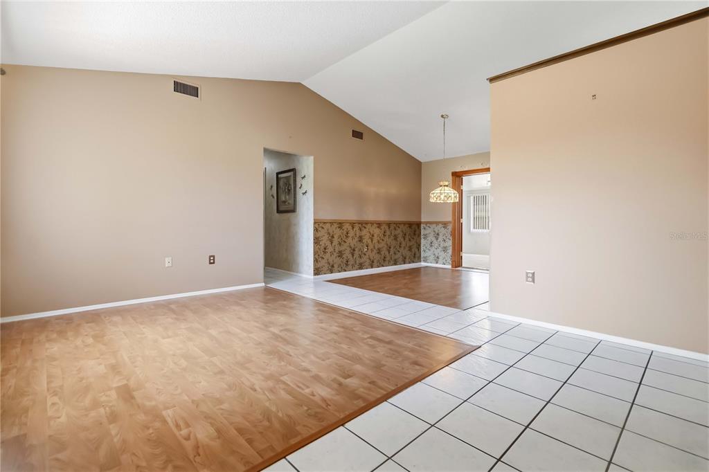 An interior view shows a living area with wood flooring, tiled entryway, and vaulted ceilings — 2415 RAINTREE LAKE CIRCLE, MERRITT ISLAND, FL