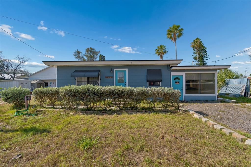 A single-story blue house with a flat roof, a front porch, and a landscaped yard — 13098 BOCA CIEGA AVENUE, MADEIRA BEACH, FL