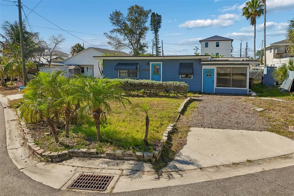 A blue single-story house features a gravel driveway, a small front lawn, and palm trees — 13098 BOCA CIEGA AVENUE, MADEIRA BEACH, FL