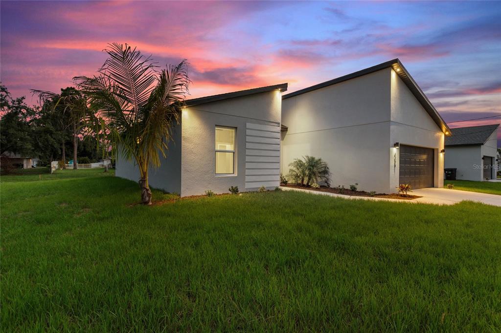 A modern single-story house with a white stucco exterior and a two-car garage at sunset — 24459 SW KINGSWAY CIRCLE, ARCADIA, FL