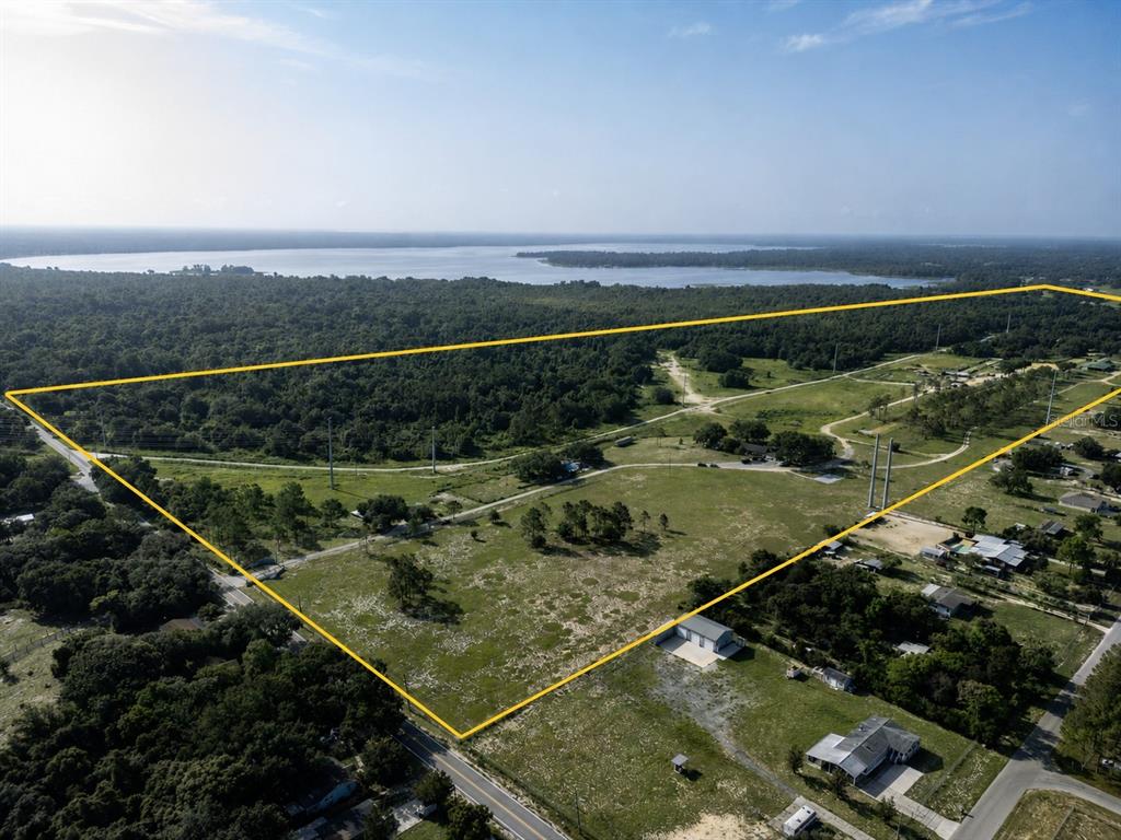 An aerial view shows a large, grassy, rectangular plot of land bordered by trees and water — 5555 E HINSON AVENUE, HAINES CITY, FL
