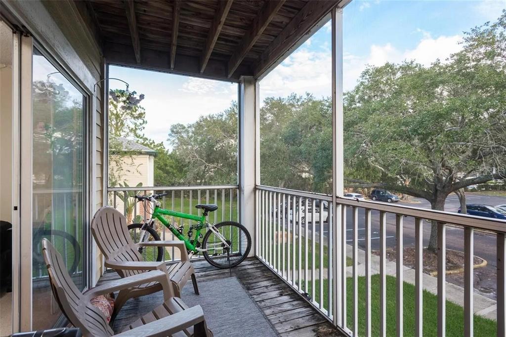 A screened-in balcony features two wooden chairs, a green bicycle, and a view of trees — 4107 CHATHAM OAK COURT UNIT 313, TAMPA, FL