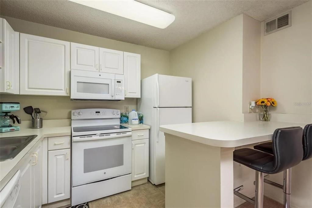 A kitchen features white cabinetry, white appliances, a breakfast bar, and two black stools — 4107 CHATHAM OAK COURT UNIT 313, TAMPA, FL