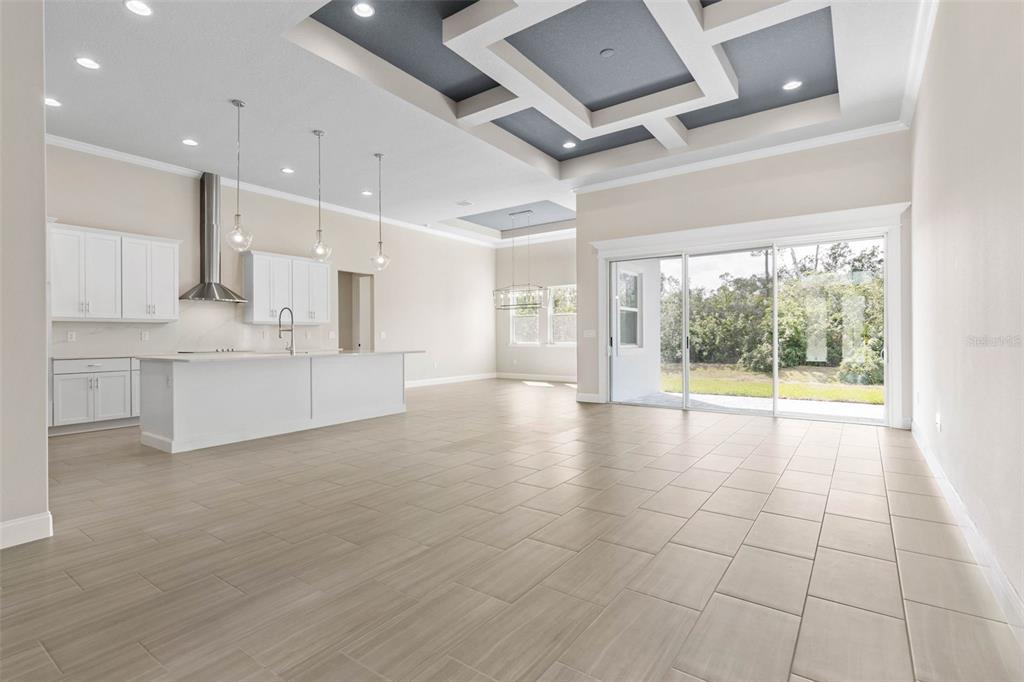 A bright, open-concept kitchen and living area features white cabinetry, tile flooring, and tray ceilings — 103 HERON DRIVE, PALM COAST, FL