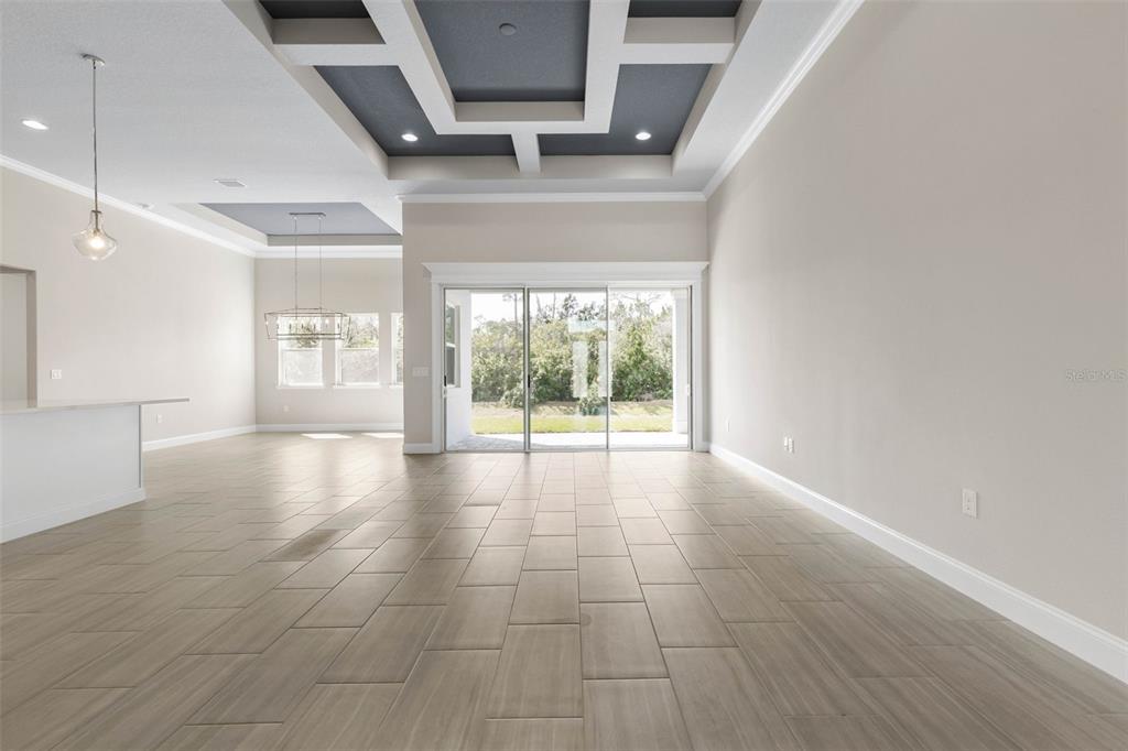 An open-concept living area features light-colored tile flooring, a coffered ceiling, and sliding glass doors — 103 HERON DRIVE, PALM COAST, FL
