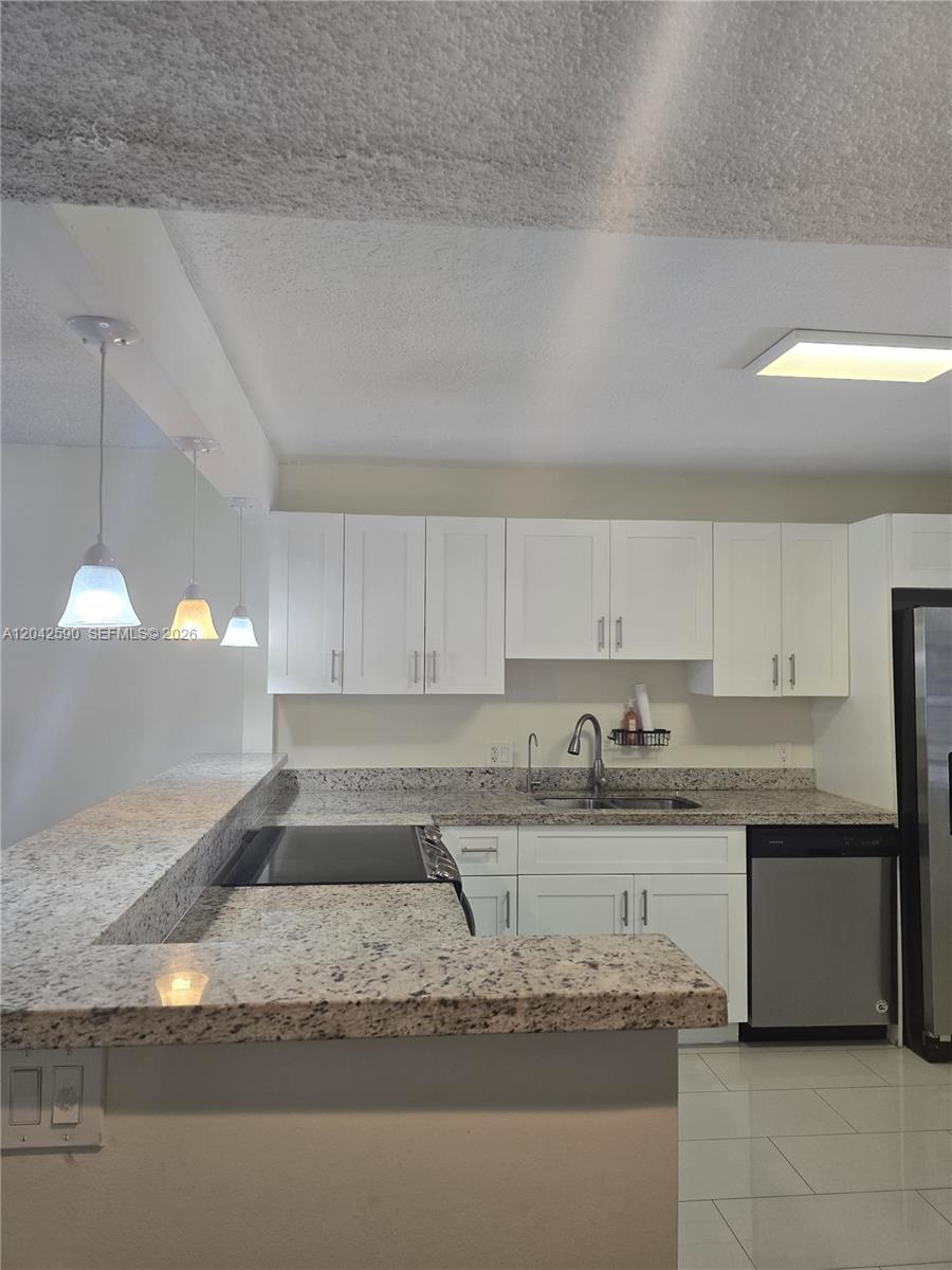 A kitchen features white cabinets, granite countertops, stainless steel appliances, and three pendant lights — 16581 Blatt Blvd # 104, Weston FL 33326, WESTON, FL