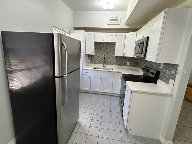A kitchen features white cabinets, stainless steel appliances, and a gray patterned tile backsplash — 1915 MORNING DRIVE, ORLANDO, FL