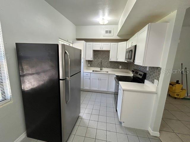 A kitchen features white cabinets, stainless steel appliances, a tiled backsplash, and light floor tiles — 1915 MORNING DRIVE, ORLANDO, FL