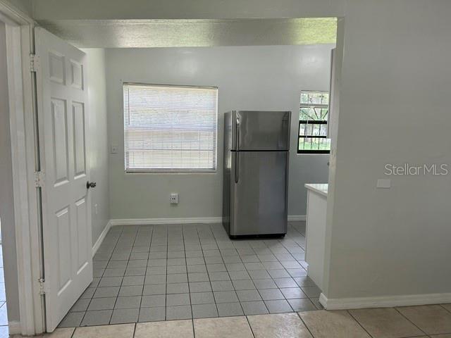 A kitchen area features a stainless steel refrigerator, tiled flooring, and a window with blinds — 1915 MORNING DRIVE, ORLANDO, FL