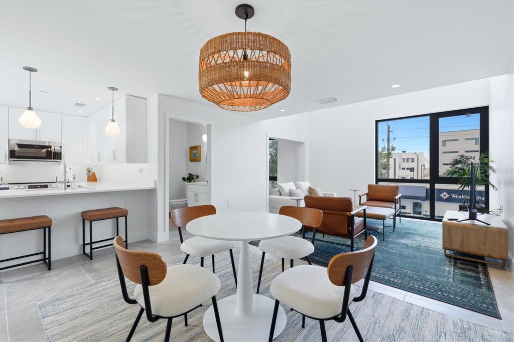 An open-concept kitchen and dining area features white cabinetry, a woven pendant light, and furniture — 1558 4TH STREET UNIT 216, SARASOTA, FL