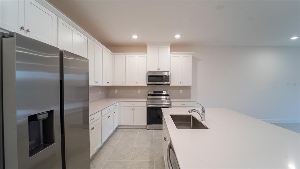 A modern kitchen features white cabinetry, stainless steel appliances, and a large central island — 4887 CROSS PRAIRIE PARKWAY, ST CLOUD, FL