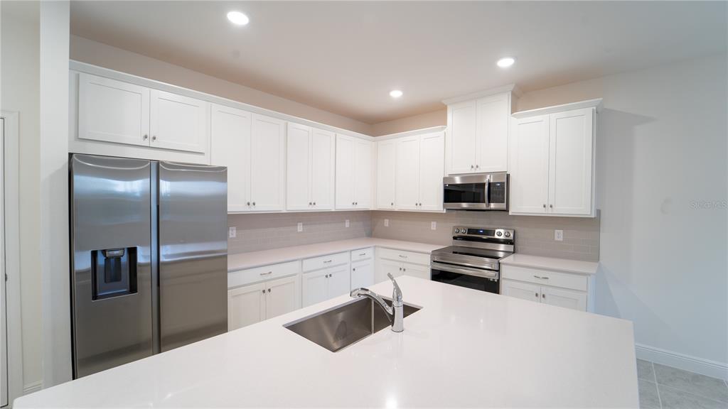 A modern kitchen features white cabinets, stainless steel appliances, and a large quartz-topped island — 4887 CROSS PRAIRIE PARKWAY, ST CLOUD, FL