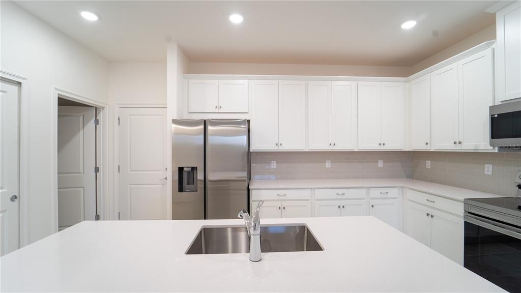 A modern kitchen features white cabinets, stainless steel appliances, and a central island with sink — 4887 CROSS PRAIRIE PARKWAY, ST CLOUD, FL